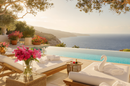 Vue aérienne d'une plage paradisiaque en Crète, avec des transats et un parasol rose, illustrant une ambiance estivale luxueuse et relaxante.